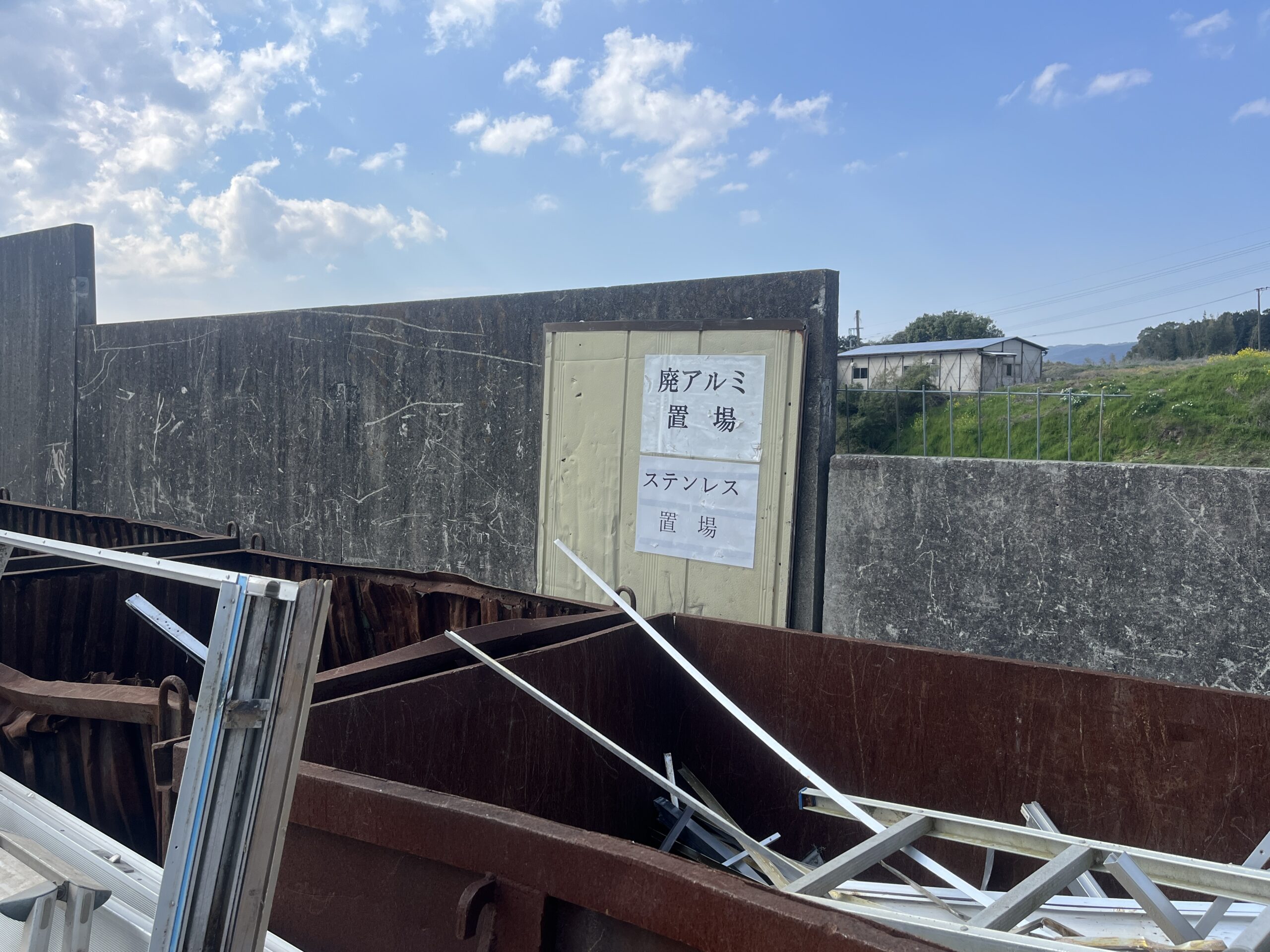 廃アルミ置場・ステンレス置場の看板と廃金属類が収納されたコンテナ