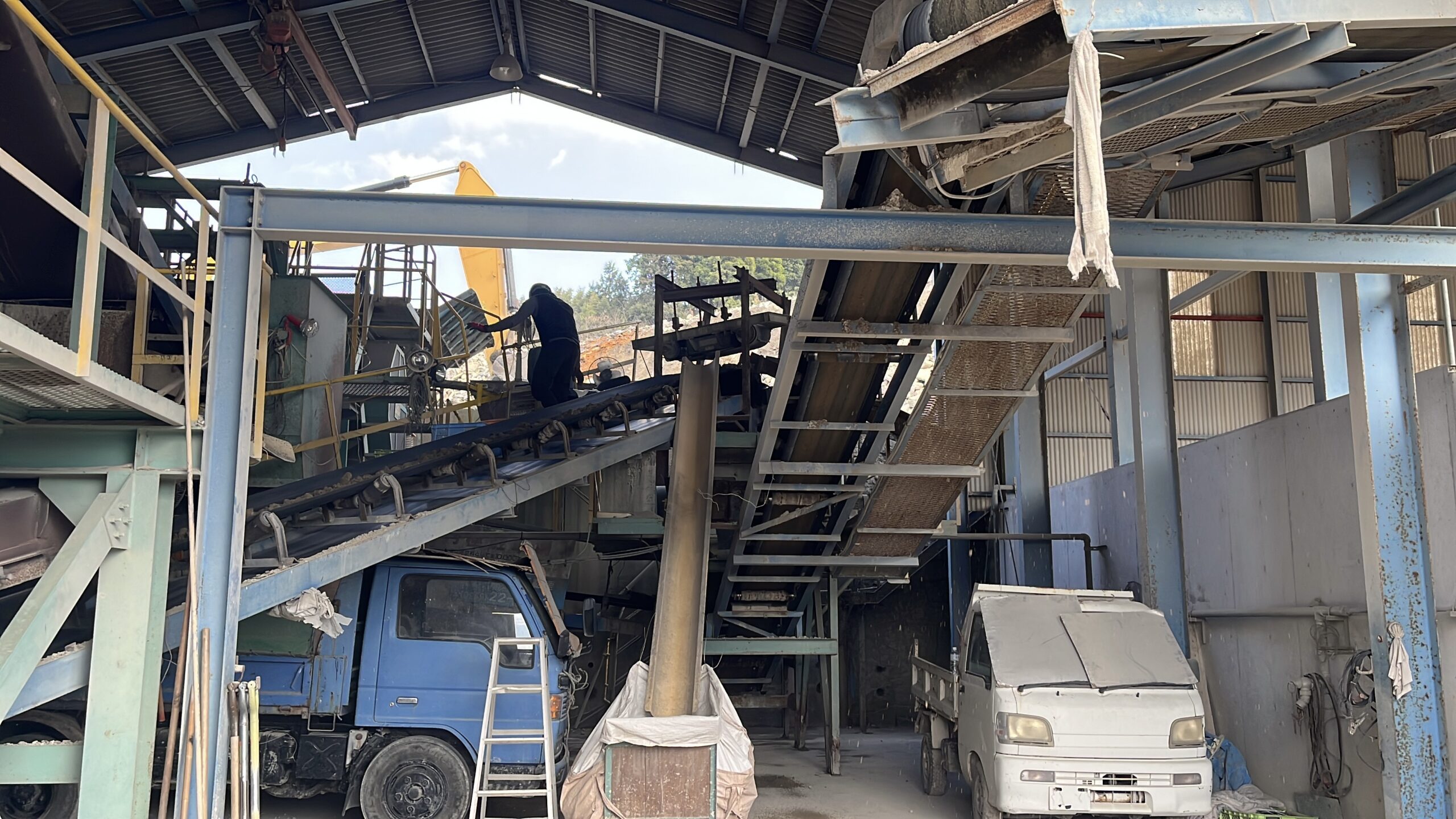 リサイクルクリーンセンターの破砕ライン全景。作業員がベルトコンベア上で搬送状況を確認している様子